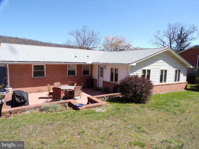 back of property featuring a patio area, a shingled roof, brick siding, and a yard