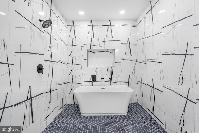 bathroom with recessed lighting, a freestanding tub, a marble finish shower, and tile walls