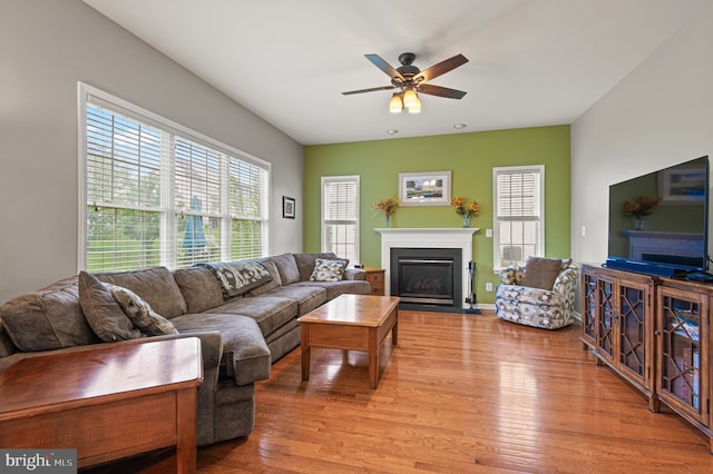 living room with a fireplace with flush hearth, a ceiling fan, and wood finished floors