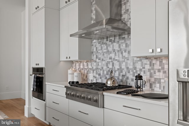 101 N Queen St Unit 402, Lancaster, PA 17603 - kitchen with wall chimney range hood, decorative backsplash, appliances with stainless steel finishes, and white cabinets