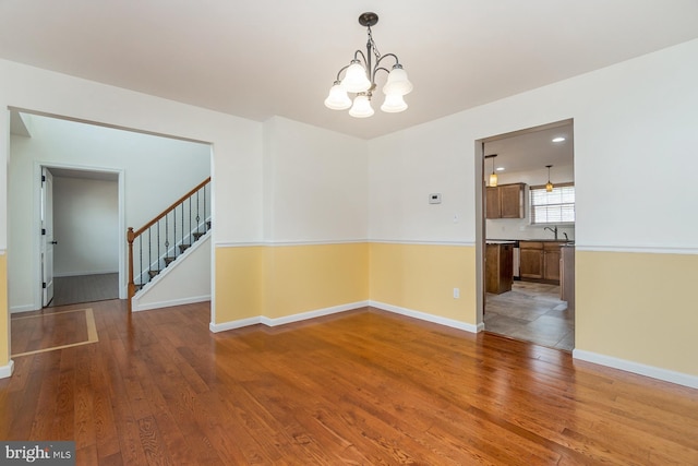 unfurnished room featuring baseboards, wood finished floors, a notable chandelier, and stairway
