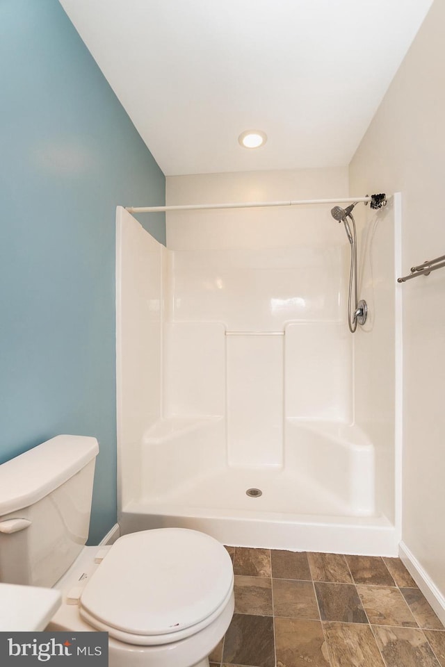 bathroom with stone finish flooring, toilet, and a shower