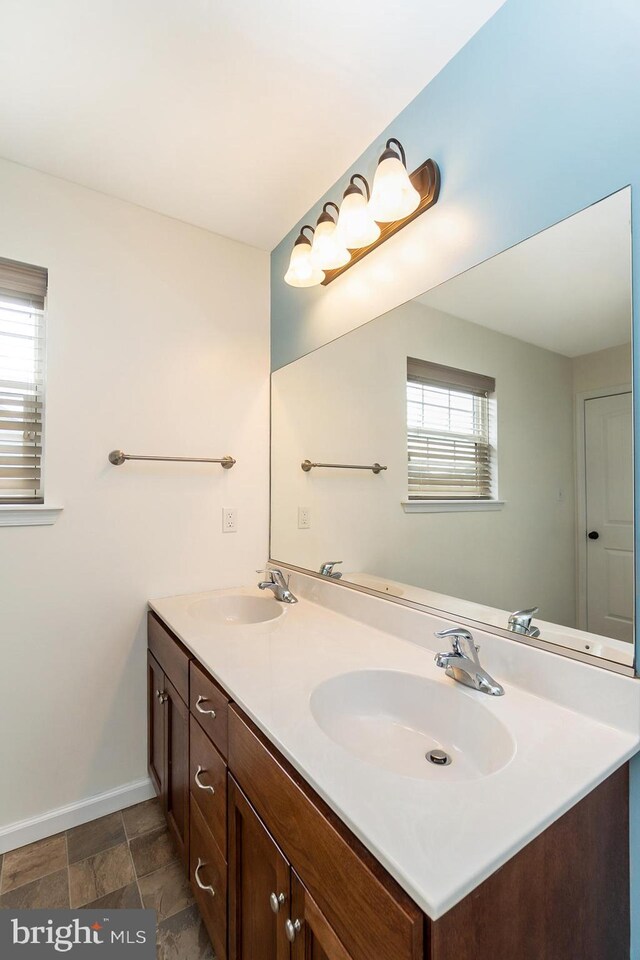 full bathroom with baseboards, stone finish floor, a sink, and double vanity