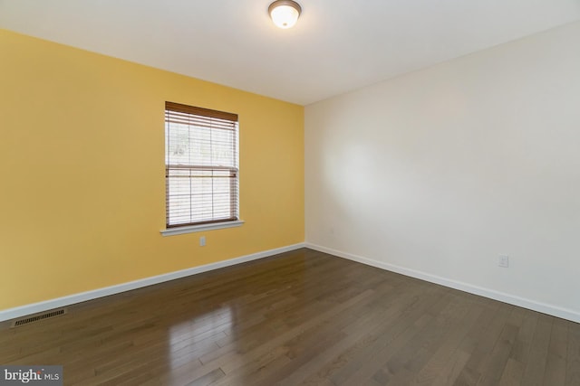 empty room featuring dark wood finished floors, visible vents, and baseboards