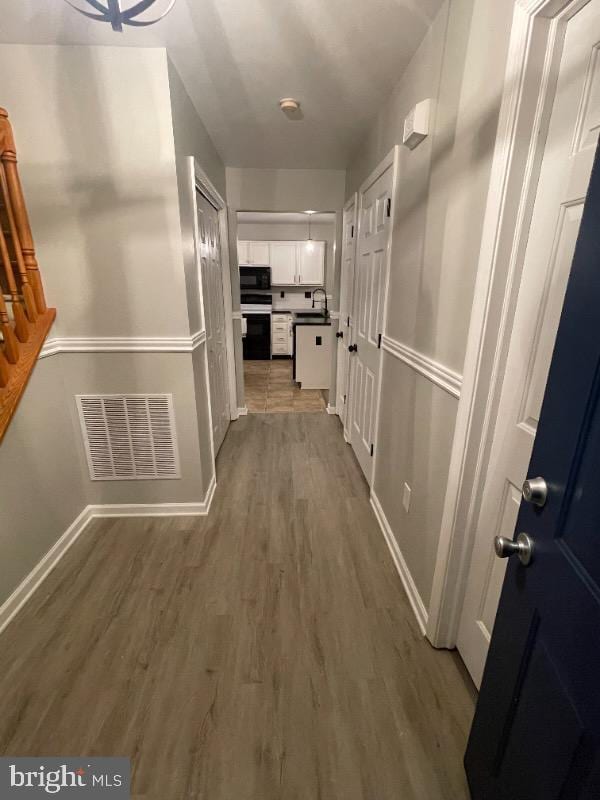 hallway with wood finished floors, baseboards, stairs, and a sink