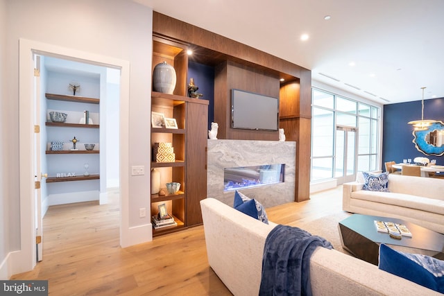 living room with recessed lighting, a premium fireplace, built in features, and light wood-style flooring