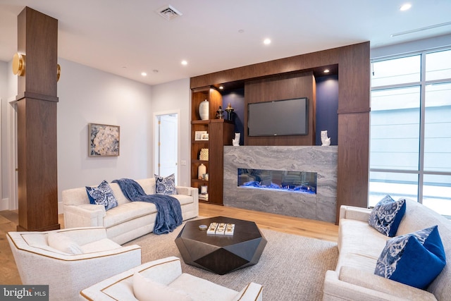 living room with a high end fireplace, recessed lighting, visible vents, and wood finished floors