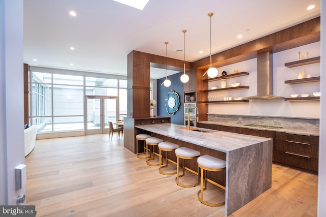bar with pendant lighting, a sink, light wood-style floors, stainless steel gas stovetop, and wall chimney exhaust hood