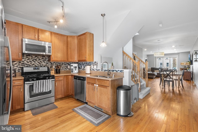 kitchen featuring a sink, light wood-style floors, a peninsula, appliances with stainless steel finishes, and open floor plan