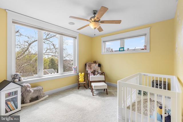carpeted bedroom featuring a crib, a ceiling fan, and baseboards