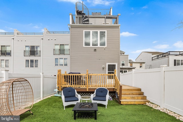 rear view of property featuring a fenced backyard, a lawn, an outdoor fire pit, and a deck