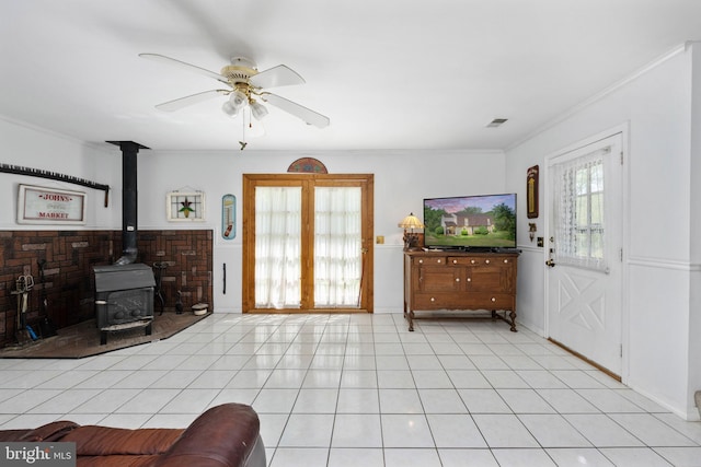 living room with ceiling fan, visible vents, a wood stove, ornamental molding, and light tile patterned flooring