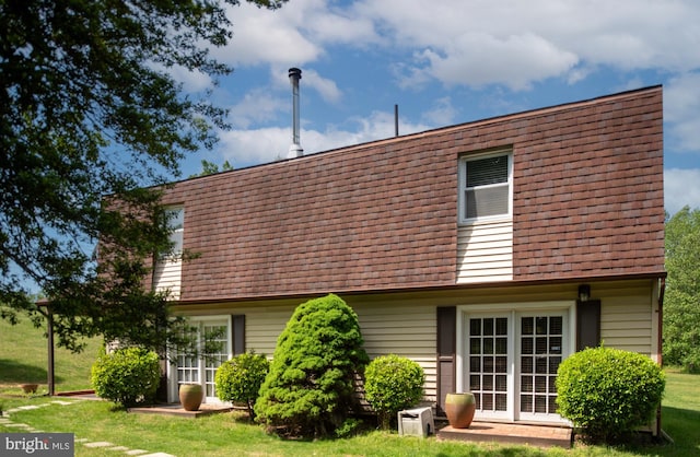 rear view of property with a yard, mansard roof, and a shingled roof