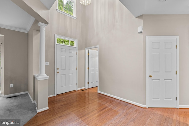 foyer featuring ornate columns, plenty of natural light, light wood-type flooring, a high ceiling, and ornamental molding