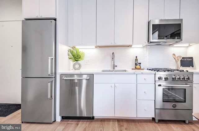 kitchen with white cabinets, stainless steel appliances, a sink, light wood-type flooring, and light countertops