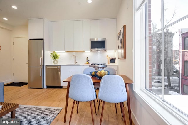 kitchen featuring white cabinets, light wood finished floors, stainless steel appliances, backsplash, and a sink