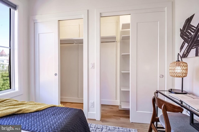 bedroom with light wood-style floors, two closets, and baseboards
