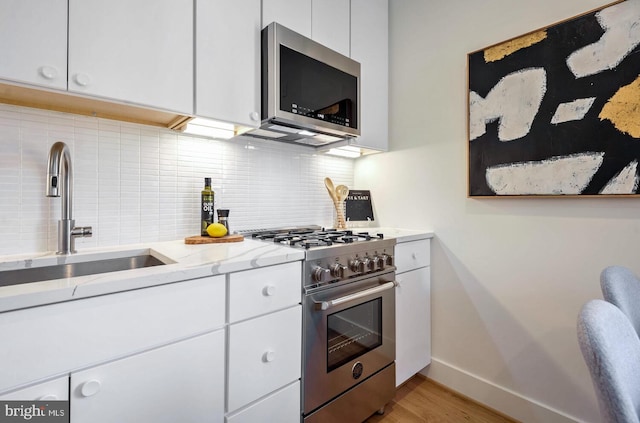 kitchen with a sink, decorative backsplash, light wood-type flooring, white cabinetry, and appliances with stainless steel finishes