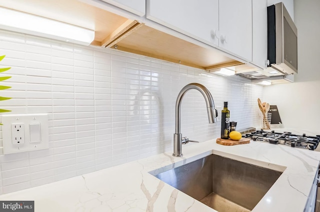 interior details featuring stainless steel microwave, backsplash, light stone counters, and a sink