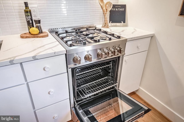 room details featuring light stone counters, decorative backsplash, baseboards, white cabinetry, and gas stove