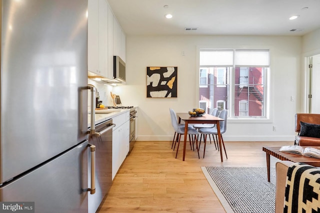 kitchen with visible vents, baseboards, white cabinetry, light wood-style floors, and appliances with stainless steel finishes