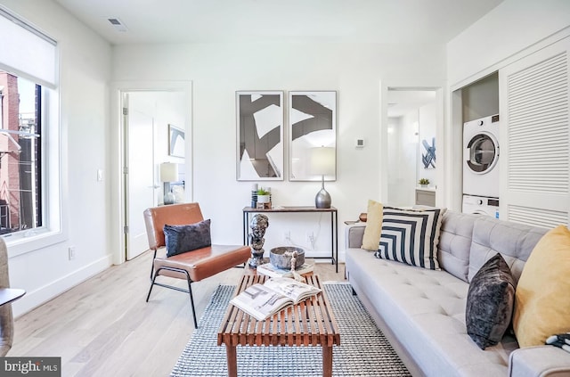 living area featuring baseboards, stacked washer and clothes dryer, visible vents, and light wood-style floors