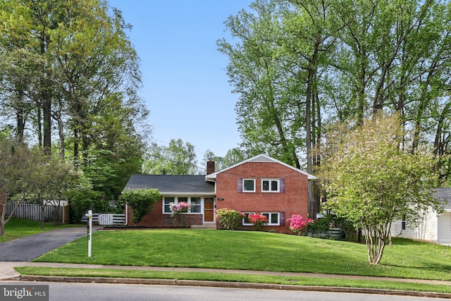 tri-level home featuring a front lawn, a chimney, aphalt driveway, and brick siding