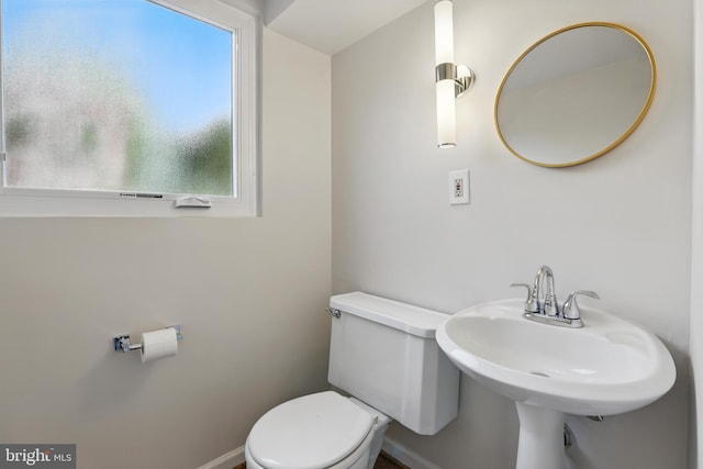 half bath with baseboards, toilet, and a sink