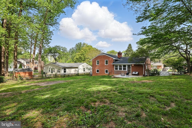 rear view of property with a chimney, a fenced backyard, brick siding, a patio area, and a lawn