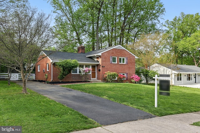 tri-level home featuring a chimney, brick siding, fence, and a front yard