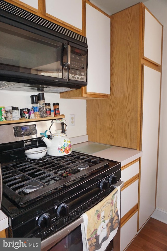 kitchen featuring wood finished floors, black microwave, gas range, light countertops, and white cabinets