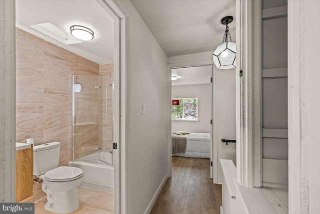 full bathroom with toilet, ensuite bathroom, baseboards, shower / washtub combination, and hardwood / wood-style flooring
