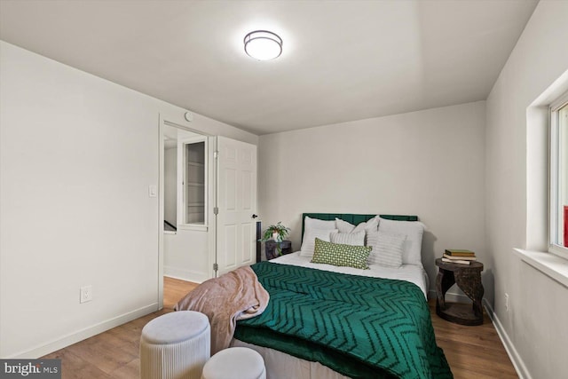 bedroom with wood finished floors, baseboards, and multiple windows