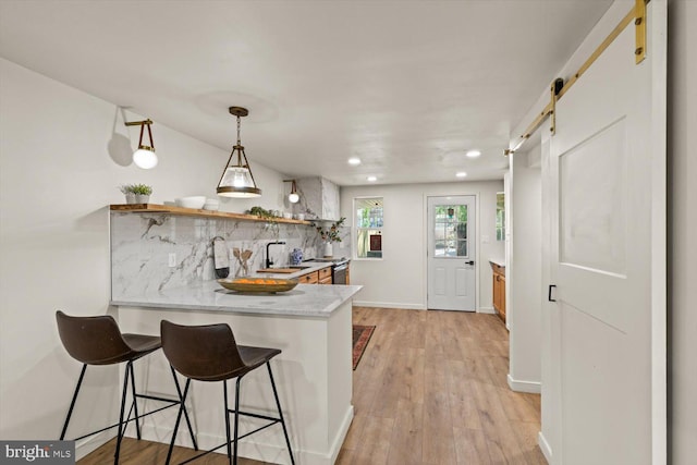 kitchen with a barn door, backsplash, light countertops, open shelves, and a peninsula