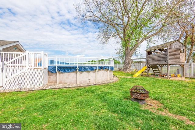 view of yard with a wooden deck, a fenced in pool, a fenced backyard, a playground, and a fire pit