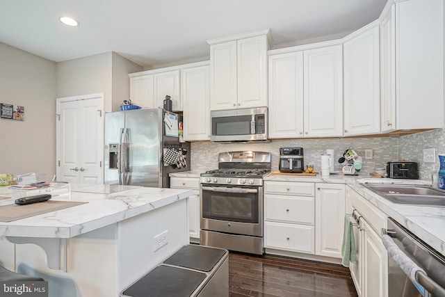 kitchen with white cabinets, appliances with stainless steel finishes, a sink, decorative backsplash, and dark wood-style floors