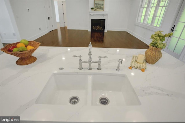 room details with wood finished floors, a fireplace, baseboards, light stone counters, and a sink