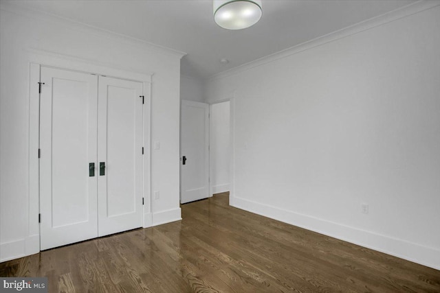 unfurnished bedroom featuring baseboards, ornamental molding, wood finished floors, and a closet