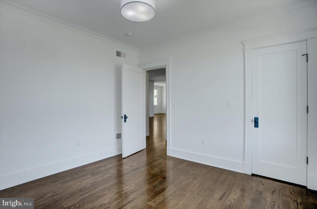 unfurnished bedroom featuring visible vents, ornamental molding, baseboards, and wood finished floors
