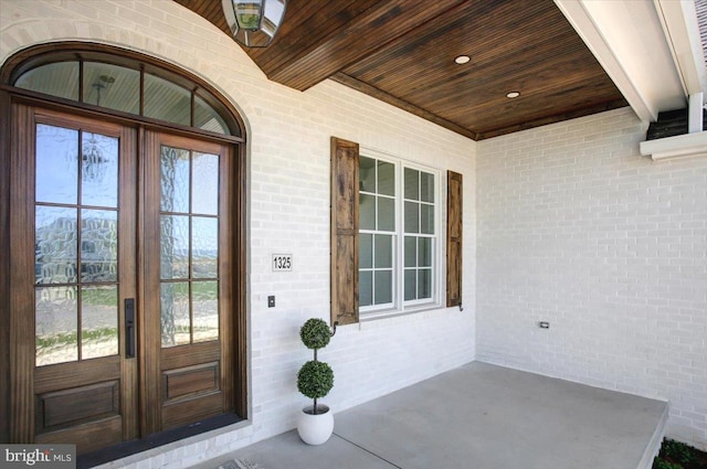 entrance to property featuring covered porch, brick siding, and french doors