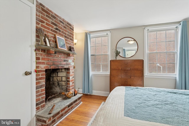 bedroom featuring baseboards, a brick fireplace, and wood finished floors