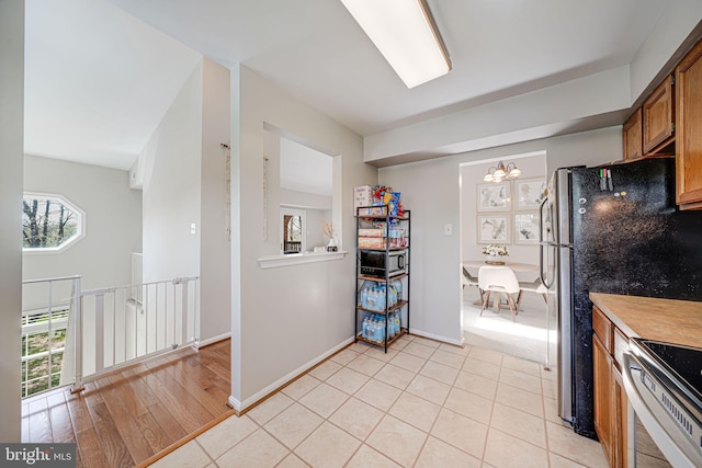 8818 Tanglewood Ln, Manassas, VA 20110 - kitchen featuring brown cabinets, stainless steel electric range, light tile patterned flooring, an inviting chandelier, and light countertops