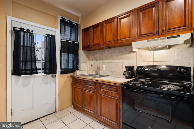 kitchen with black range with electric stovetop, under cabinet range hood, a sink, tile counters, and backsplash
