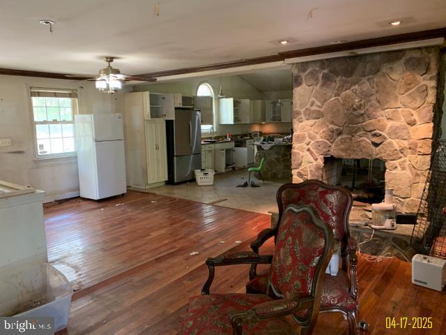 living room with a fireplace, ornamental molding, a ceiling fan, and light wood-style flooring