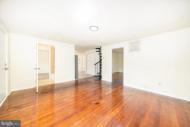 unfurnished living room with baseboards, visible vents, stairway, and wood-type flooring