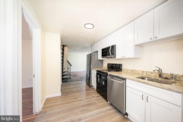 kitchen featuring white cabinets, a sink, stainless steel appliances, light wood-type flooring, and light stone countertops