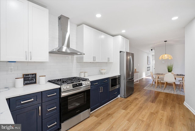 kitchen with white cabinets, appliances with stainless steel finishes, wall chimney exhaust hood, backsplash, and blue cabinets