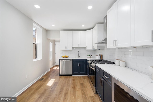 kitchen featuring a sink, wall chimney exhaust hood, appliances with stainless steel finishes, and white cabinetry