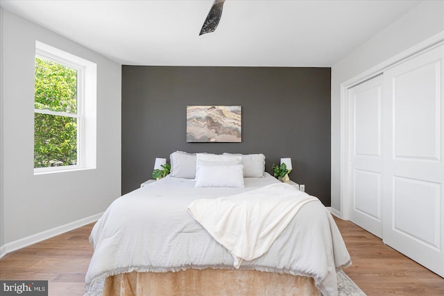 bedroom with baseboards, an accent wall, a closet, and wood finished floors
