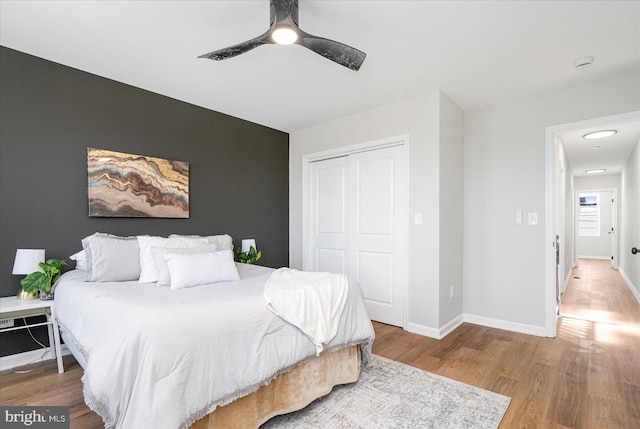 bedroom with baseboards, ceiling fan, wood finished floors, and a closet